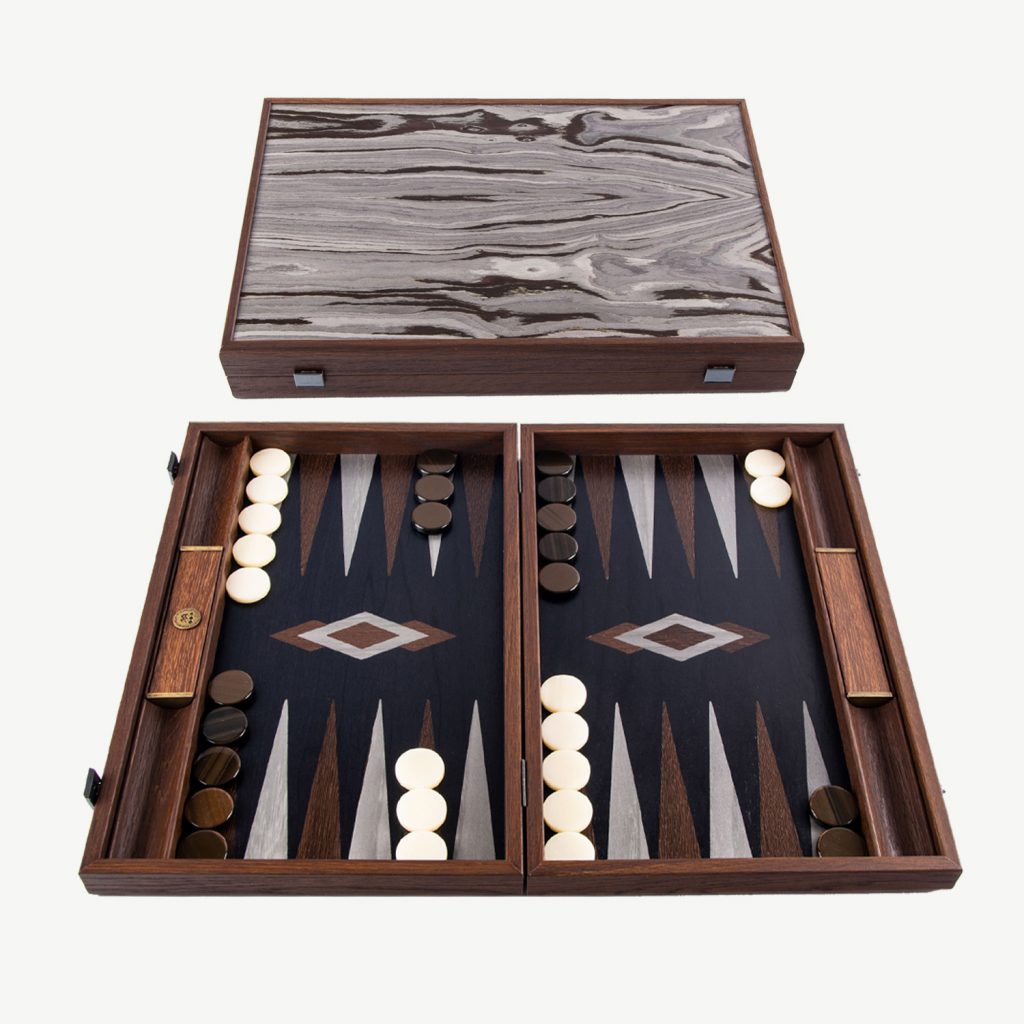 This Fossil Forest Luxury Backgammon Set from the world famous Manopoulos in Greece is the perfect companion for a game of backgammon when you want to spend quality time with your loved ones.

ABOUT MANOPOULOS - Manopoulos, a renowned Greek manufacturer, specializes in creating exquisite Backgammon sets that have gained global recognition. They have been handcrafting quality board games since 1970. Their exceptional wooden and leatherette sets seamlessly blend elegant design with sturdy construction, providing an unmatched gaming experience. Additionally, they offer uniquely designed Backgammon sets that cater to those who seek a distinctive and standout board for their Backgammon games.

FOSSIL FOREST: This Luxury Backgammon board is classic in Backgammon board design but especially stands out with the Architectural wood veneer producing a creative atmosphere. The irregular shape and colour intensity of the dark brown core contrasting silky shades of Grey tones, give the veneer figure a temperamental character. The set is handcrafted using the art of Marquetry from Black Oak with Wenge and grey points. Each backgammon set made is UNIQUE.

DIMENSIONS - Board Size is 19inch x 12 inch (48cm x 30 cm) when closed. Weight 2.8 kg.  Side racks are built into this high quality set which are great for game organisation either for dice rolling or for checker placement.

The set includes

 	30 mother of pearl checkers (15 Brown & 15 White)
 	4 dice
 	1 Doubling cube
 	1 set of Wooden Dice Cups
