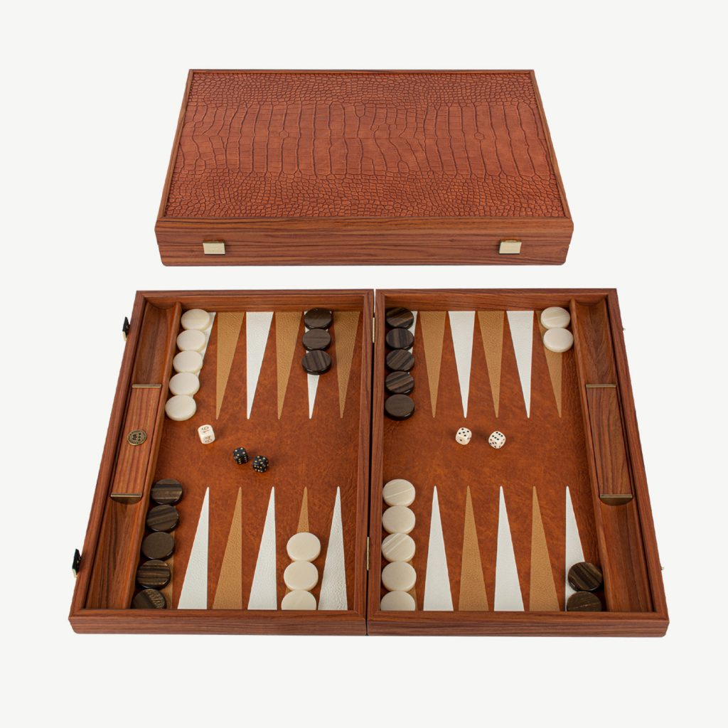 One of our Buyers favourites this Crocodile Tote Luxury Backgammon Set with side racks is a superior Backgammon set and a touch above the rest.

ABOUT MANOPOULOS - Manopoulos, a renowned Greek manufacturer, specializes in creating exquisite Backgammon sets that have gained global recognition. They have been handcrafting quality board games since 1970. Their exceptional wooden and leatherette sets seamlessly blend elegant design with sturdy construction, providing an unmatched gaming experience. Additionally, they offer uniquely designed Backgammon sets that cater to those who seek a distinctive and standout board for their Backgammon games.

CROCODILE TOTE: This Luxury Backgammon board is made in a warm caramel brown colour which is one of our customers favourites. The set is inlaid with a Premium quality ECO LEATHER to give a fake Crocodile skin finish on the exterior and a sumptuous warm Caramel Brown Leather playing surface in the Interior. The Leatherette has the advantage of noise reduction and durability. The set is handcrafted using the art of Marquetry. Each backgammon set made is UNIQUE.

DIMENSIONS - Board Size is 19inch x 12 inch (48cm x 30 cm) when closed. Weight 2.8 kg.  Side racks are built in to this high quality set which are great for game organisation either for dice rolling or for checker placement.

SET INCLUDES : 30 mother of pearl checkers (15 Brown & 15 White), 4 dice, 1 black doubling cube, 1 set of Wooden Dice Cups. Is packed in a Manopoulos gift box

PERFECT PRESENT – Sent out in a Manopoulos Gift box so can be given as a perfect present for Christmas or Birthdays.