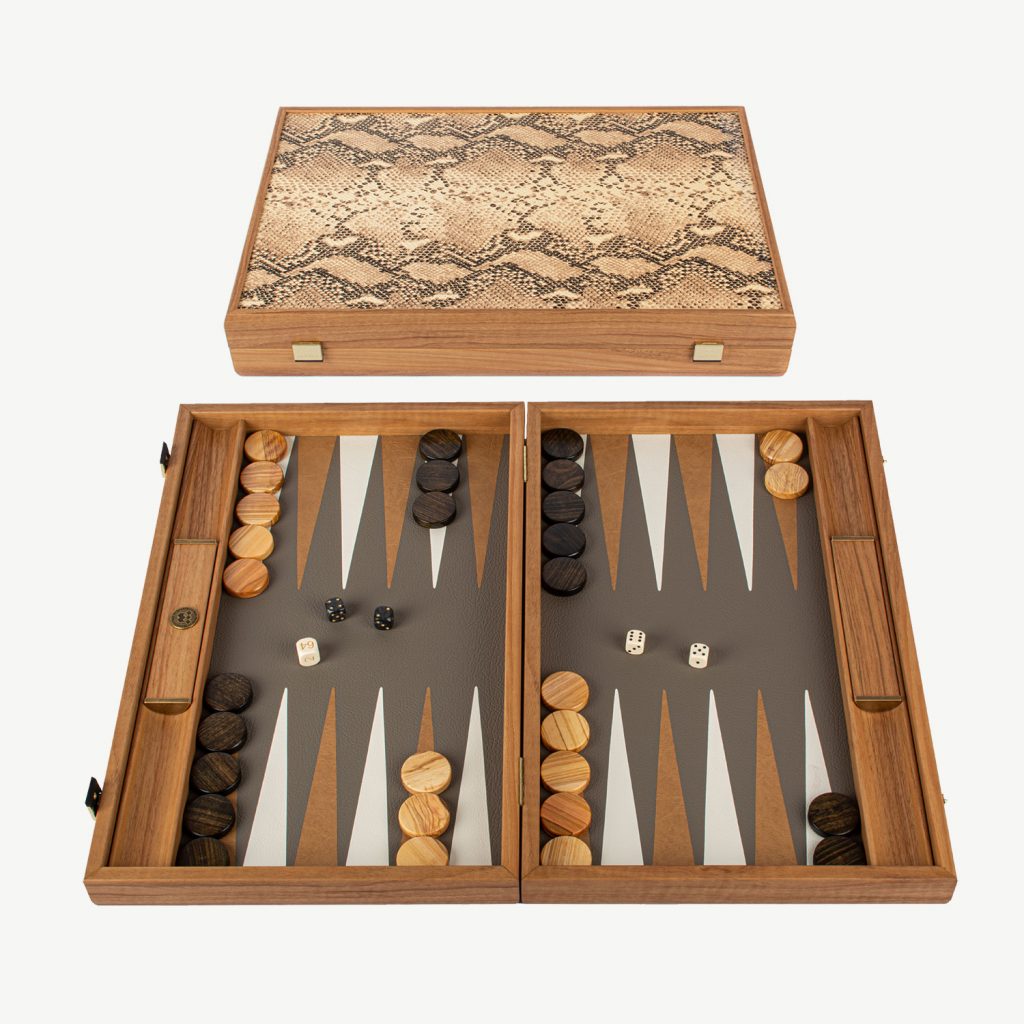 This is the Ultimate Luxury Backgammon Set with side racks and will turn heads as you play.

ABOUT MANOPOULOS - Manopoulos, a renowned Greek manufacturer, specializes in creating exquisite Backgammon sets that have gained global recognition. They have been handcrafting quality board games since 1970. Their exceptional wooden and leatherette sets seamlessly blend elegant design with sturdy construction, providing an unmatched gaming experience. Additionally, they offer uniquely designed Backgammon sets that cater to those who seek a distinctive and standout board for their Backgammon games.

SNAKE TOTE - This Superior Luxury Backgammon board has a unique look and is handcrafted with our highest level of craftsmanship. The combination of the rigid wood frame with the finest Italian leather exterior surface is designed especially for the most demanding backgammon players. The inlaid playing field is perfectly assembled and crafted with a special German made ECO-LEATHER in Grey-Beige with Light Brown and White points. The finest Italian leather exterior surface made to resemble fake Snake skin is designed for a lifetime of enjoyment.. The Leatherette has the advantage of noise reduction and durability. The set is handcrafted showing quality in design and therefore each backgammon set made is UNIQUE.

DIMENSIONS - Board Size is 19inch x 12 inch (48cm x 30 cm) when closed. Weight 2.8 kg.  Side racks are built in to this high quality set which are great for game organisation either for dice rolling or for checker placement.

SET INCLUDES : 30 mother of pearl checkers (15 Brown & 15 Natural Light Wood), 4 dice, 1 black doubling cube, 1 set of Wooden Dice Cups. Is packed in a Manopoulos gift box

PERFECT PRESENT – Sent out in a Manopoulos Gift box so can be given as a perfect present for Christmas or Birthdays.