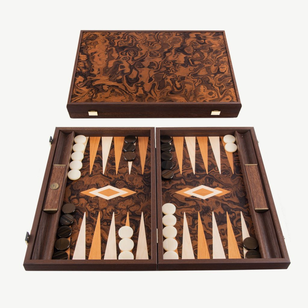 This Californian Walnut Burl Luxury Backgammon Set is stand out beautiful.

ABOUT MANOPOULOS - Manopoulos, a renowned Greek manufacturer, specializes in creating exquisite Backgammon sets that have gained global recognition. They have been handcrafting quality board games since 1970. Their exceptional wooden and leatherette sets seamlessly blend elegant design with sturdy construction, providing an unmatched gaming experience. Additionally, they offer uniquely designed Backgammon sets that cater to those who seek a distinctive and standout board for their Backgammon games.

CALIFORNIAN WALNUT BURL: For this Luxury Backgammon Board we love the gorgeous look of the California walnut burl is especially vibrant. The colour of the heartwood tends to be more chocolate brown while the European variety is more reddish brown. Lively figures in dark brown to black wood give the veneer a mystical aura. The playing field is a combination of California Walnut burl with Cherry & Oak points.This backgammon is handmade using the art of marquetry (also spelled as marqueterie) which is the art and craft of applying pieces of veneer to a structure to form decorative patterns and designs which we use in order to create the interior design of the backgammon.

DIMENSIONS - Board Size is 19inch x 12 inch (48cm x 30 cm) when closed. Weight 2.8 kg.  Side racks are built in to this high quality set which are great for game organisation either for dice rolling or for checker placement.

SET INCLUDES : 30 mother of pearl checkers (15 Brown & 15 White), 4 dice, 1 black doubling cube, 1 set of Wooden Dice Cups.

PERFECT PRESENT – Sent out in a Manopoulos Gift box so can be given as a perfect present for Christmas or Birthdays.